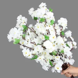 Detail shot of artificial white peach blossom branch, realistic silk flowers and green leaves.