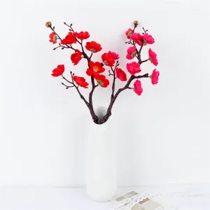 Artificial red plum blossom branch in a white vase for home and living room decor.