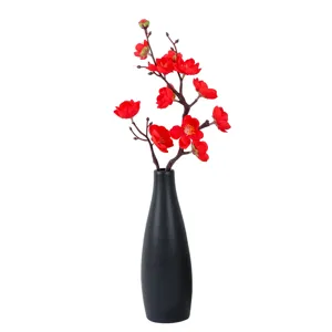 Close-up view of artificial red plum blossom branch in black vase for home decor detail.