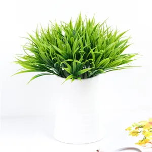 Detail view of artificial green spring grass potted in white vase for indoor home decor.