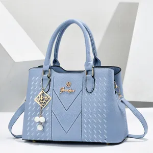 Light blue faux leather handbag detail showing metal logo emblem and elegant hanging charm.