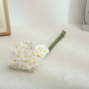 Close-up detail of white artificial daisy flower bouquet on white textured tabletop.