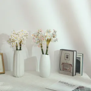 Detail shot of artificial daisy flower bouquet in white ceramic vase for chic home decoration.