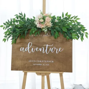 Detailed view of wooden welcome sign decorated with artificial eucalyptus leaves and pink flowers.