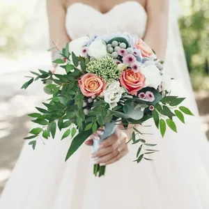 Beautiful artificial wedding bouquet detail with realistic peach roses and green leaves.