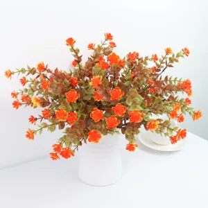 Primo piano dettagliato bouquet foglie eucalipto artificiali e fiori arancioni in vaso bianco.