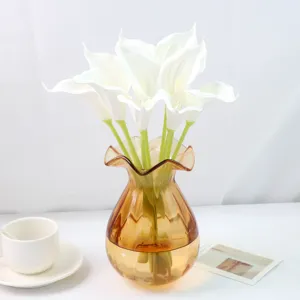 Vue détaillée de callas blanches artificielles dans un vase en verre ambré, déco florale.