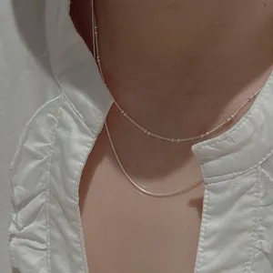 Close-up detail shot of layered silver necklaces featuring delicate snake and bead chains.