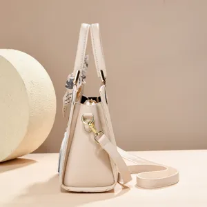 Detailed view of elegant light beige shoulder bag with scarf accessory and metal hardware.