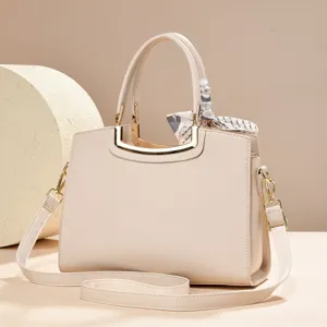Close-up detail view of the elegant beige handbag showing gold hardware and chic handle scarf.