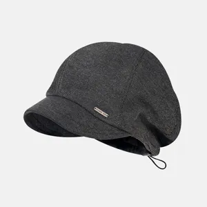 Close-up view of the dark grey knit newsboy cap showcasing the metal tag and short brim.