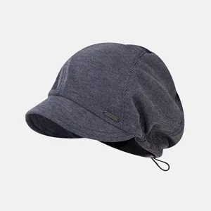 Close-up detail of the dark grey slouchy beret cap with metal badge and short brim.