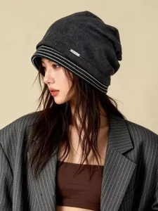 Detailansicht der stilvollen dunkelgrauen Beanie Mütze mit weißen Streifen und Metallabzeichen.