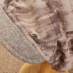 Nahaufnahme der Retro-Strickmütze im Detail, braunes Batikmuster mit Metall-Markenbuchstabe.