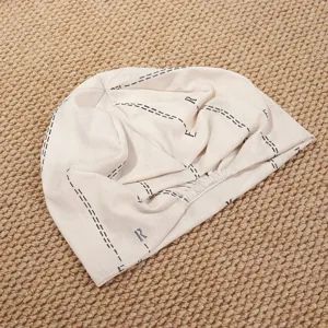 Nahaufnahme der beige Slouchy Beanie Mütze mit Buchstaben und Linien, weicher Stoff.