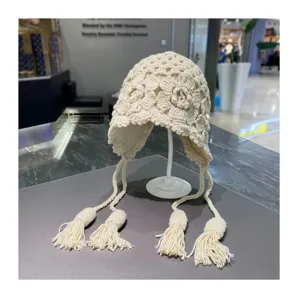 Detailansicht der handgefertigten Häkelblumen-Strickmütze mit Ohrenklappen und Quasten.