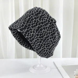 Detailed shot of black knitted bucket hat with white floral jacquard pattern on white stand.