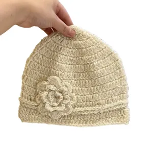 Handgemachte Häkelstrickmütze in Cremeweiß mit dekorativen Blumen und glänzenden Pailletten.