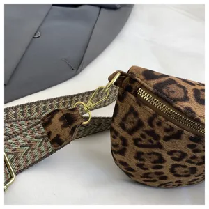 Close-up detail of stylish leopard print crossbody bag with woven strap and gold hardware.
