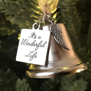 Close-up detail of a silver Christmas bell pendant with engraved metal tag and wing charm.