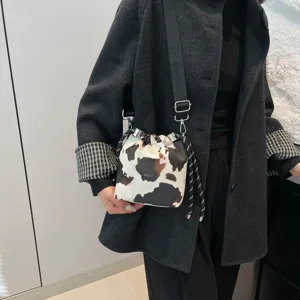Close-up of stylish cow print drawstring shoulder bag with black strap and metal hardware details.