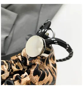 Close-up detail of leopard print clutch bag with metallic clasp and black woven drawstring.