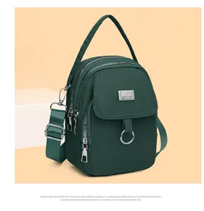 Close-up detail of dark green nylon multi-zipper crossbody bag with metal badge.