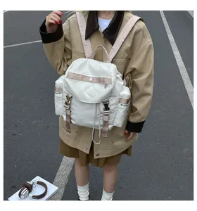 Détail de rue d'un sac à dos blanc en nylon avec rabat, boucles et poches latérales.
