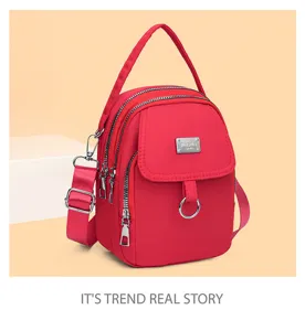 Detail view of red multi-zipper mini crossbody bag with metal badge and top handle.