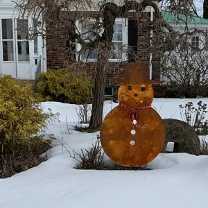 Rust metal snowman garden stake with top hat and plaid scarf for winter yard decoration.