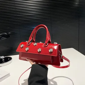 Gros plan détail sac baguette épaule cuir verni rouge avec superbes clous argentés.