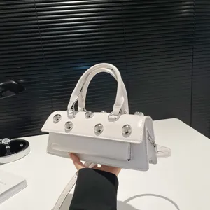 Vue détaillée du sac baguette en cuir verni blanc avec des rivets sphériques métalliques.