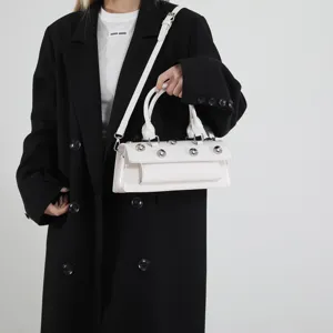 Détail de sac baguette en cuir verni blanc avec clous métalliques et poignées élégantes.