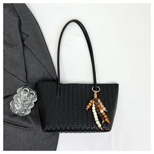 Close-up of black woven leather tote bag detail with beaded tassel charm and stylish blazer.