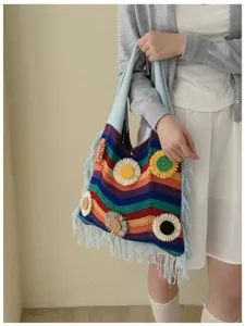 Detalle de bolso de hombro tejido con rayas de arco iris, flores en relieve y flecos.