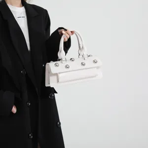 Détail de sac baguette blanc, sac à épaule chic avec rivets boules métalliques et cuir lisse.