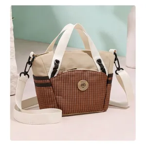 Detailed view of the brown plaid canvas mini crossbody bag with white handles and zipper pocket.