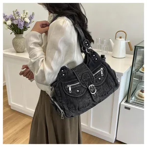 Black denim shoulder bag detail showcasing multiple zipper pockets, studs and buckle.