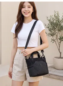 Detailed shot of a stylish black grid crossbody bag worn by a model in a minimal setting.