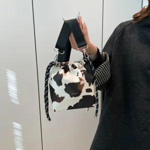 Close up of the cow print bucket bag with black strap and metallic hardware details.