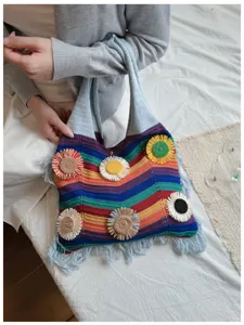Primer plano detallado del bolso de hombro de punto con rayas de arcoíris y detalles florales.