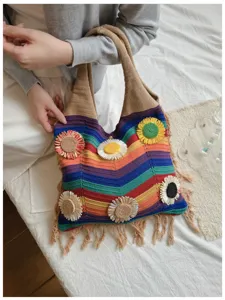 Primer plano de bolso de hombro de punto de arcoíris con aplicaciones de girasol y flecos.