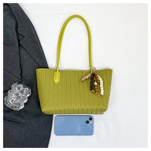 Green woven leather shoulder tote bag detail view with cute wood bead charm and props.