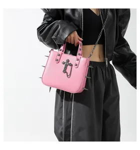 Detalle de bolso de hombro rosa gótico con colgante cruz de metal y tachuelas punk.