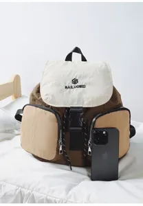 Detail shot of casual contrast-color backpack with front pockets and brand logo on bed.