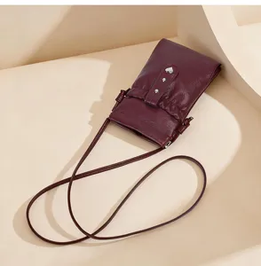 Burgundy leather crossbody phone bag with heart snap closure and thin shoulder strap.