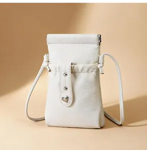 Detail shot of white crossbody phone bag, drawstring closure, metallic heart charm accent.