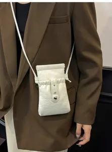 Detail view of minimalist white leather crossbody phone bag featuring a cute heart metal snap.