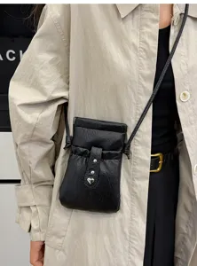 Detail view of a minimalist black leather crossbody phone bag with drawstring and heart charm.
