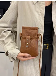 Close-up shot of the brown faux leather crossbody phone pouch with a stylish metal heart charm.